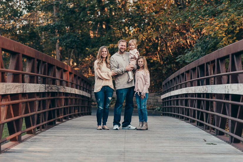 family of 4 in neutral colors and jeans standing on a bridge Cleveland Pediatricians