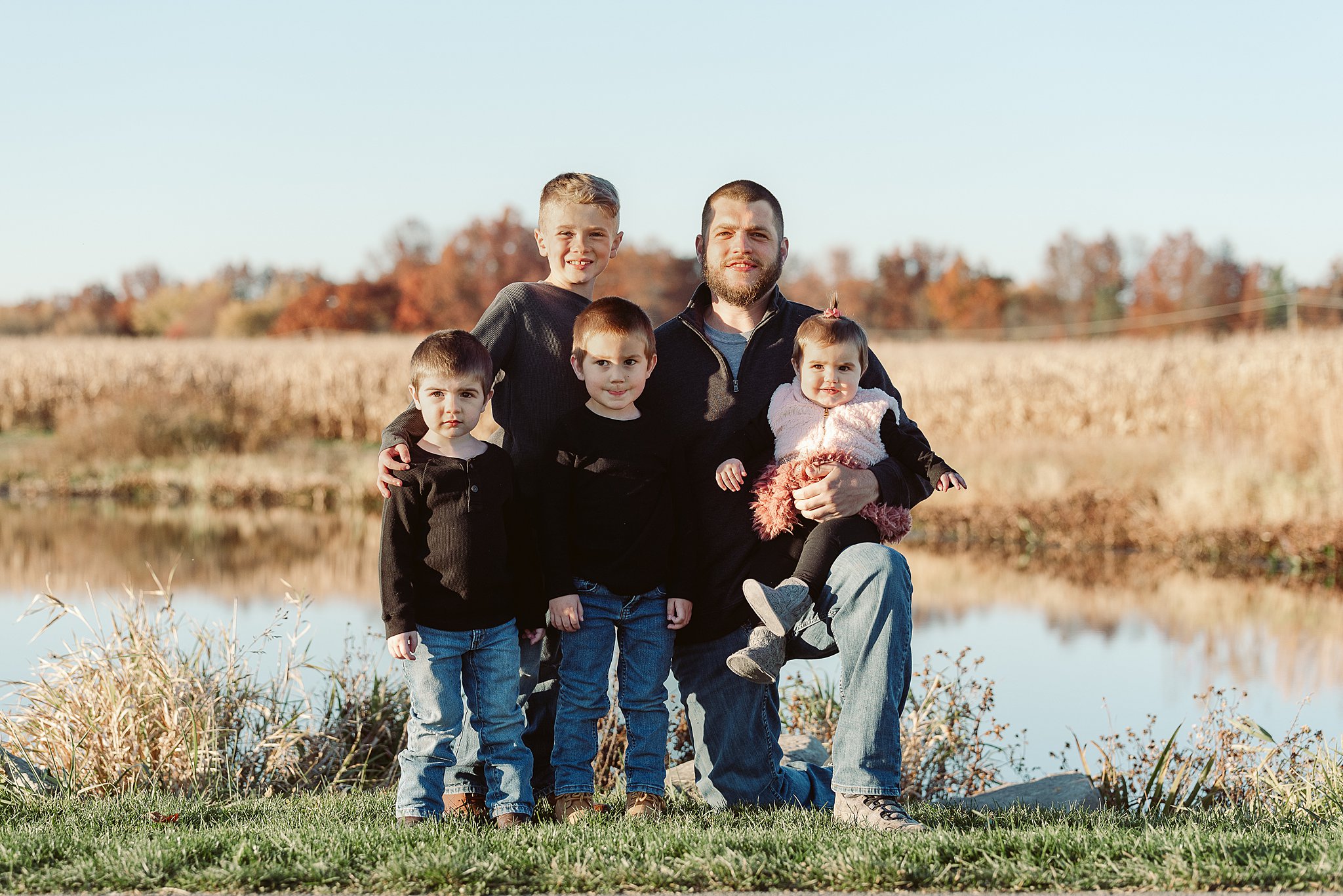 A father holds his daughter on his knee while hugging his three sons in front of a lake build a bear strongsville