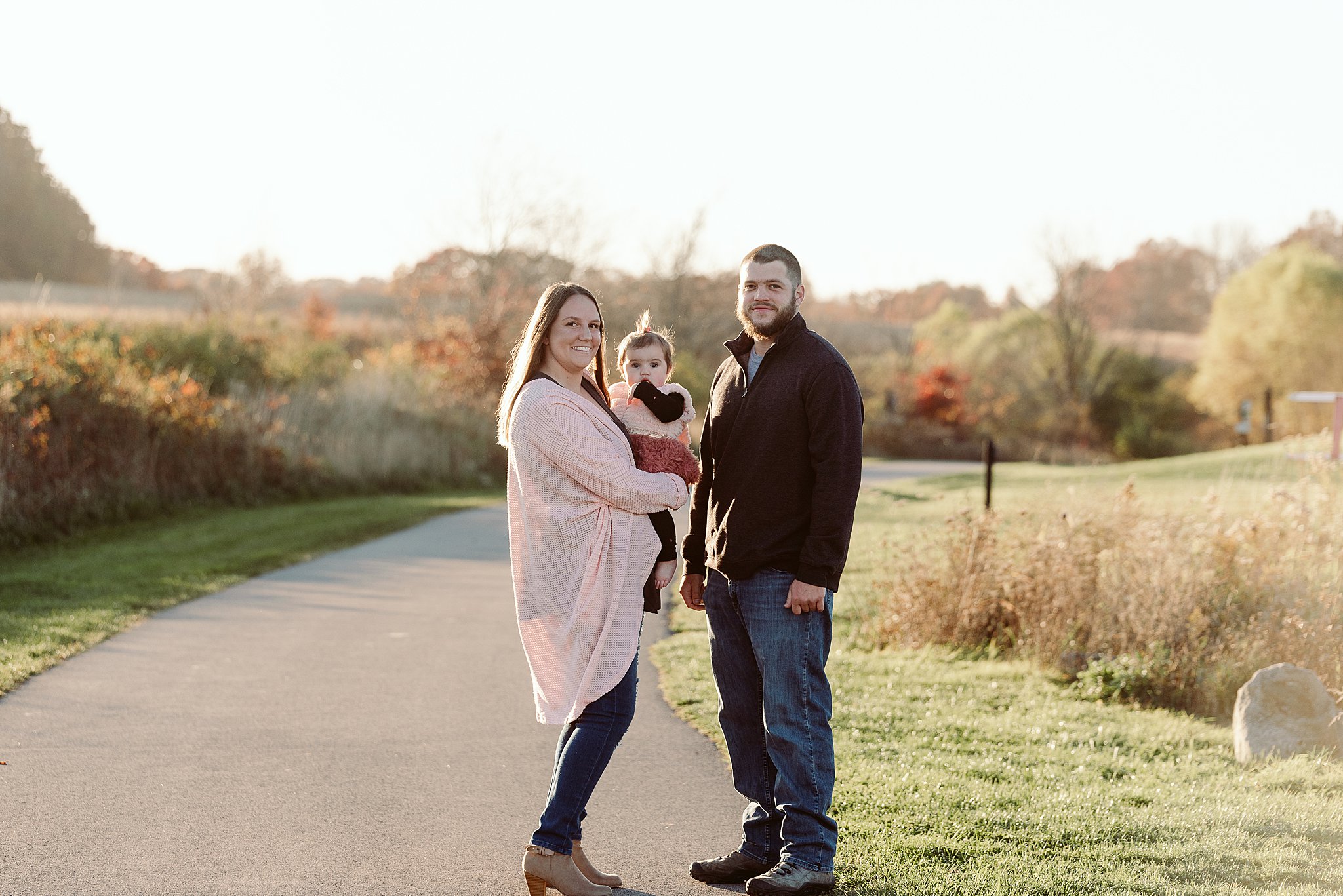 Parents stand on a park path while holding their toddler daughter build a bear strongsville