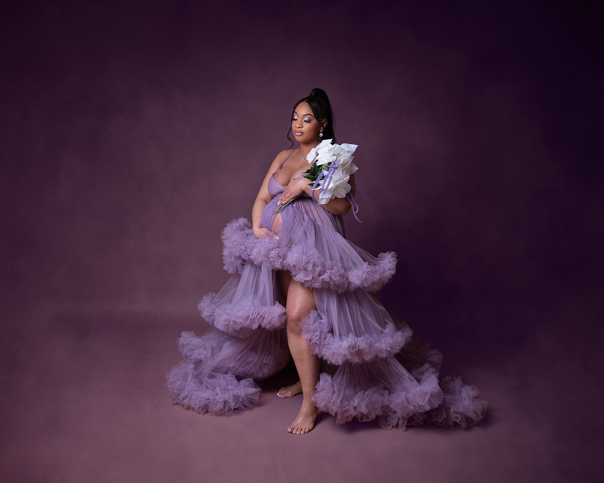 A mother to be holds her bump in a studio in a puffy purple tule maternity gown elliott cooper new albany