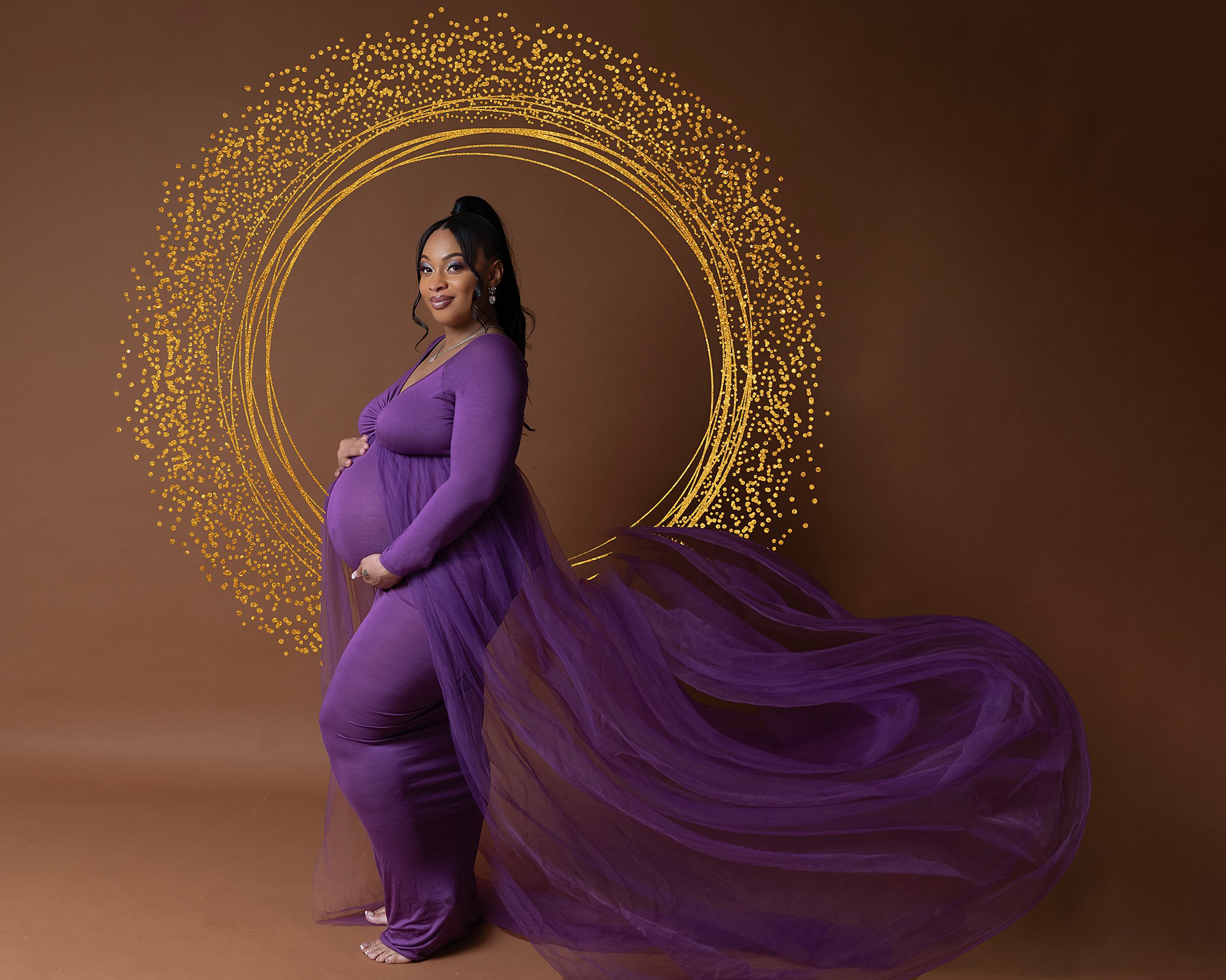 A mother to be in a purple flowing dress stands in a studio holding her bump elliott cooper new albany