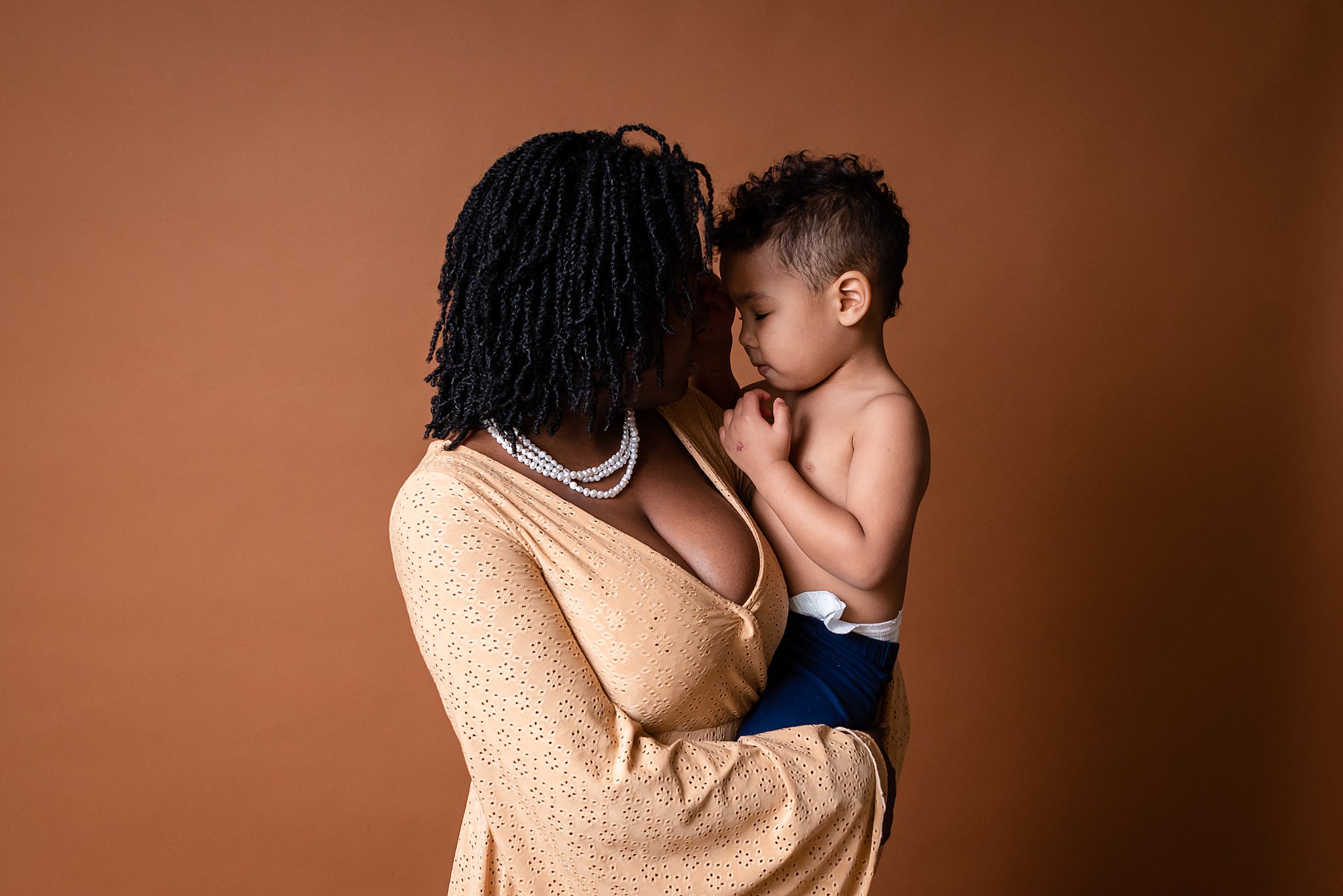 A mom stands in a studio with her toddler on her hip while he plays with her hair little bee creations