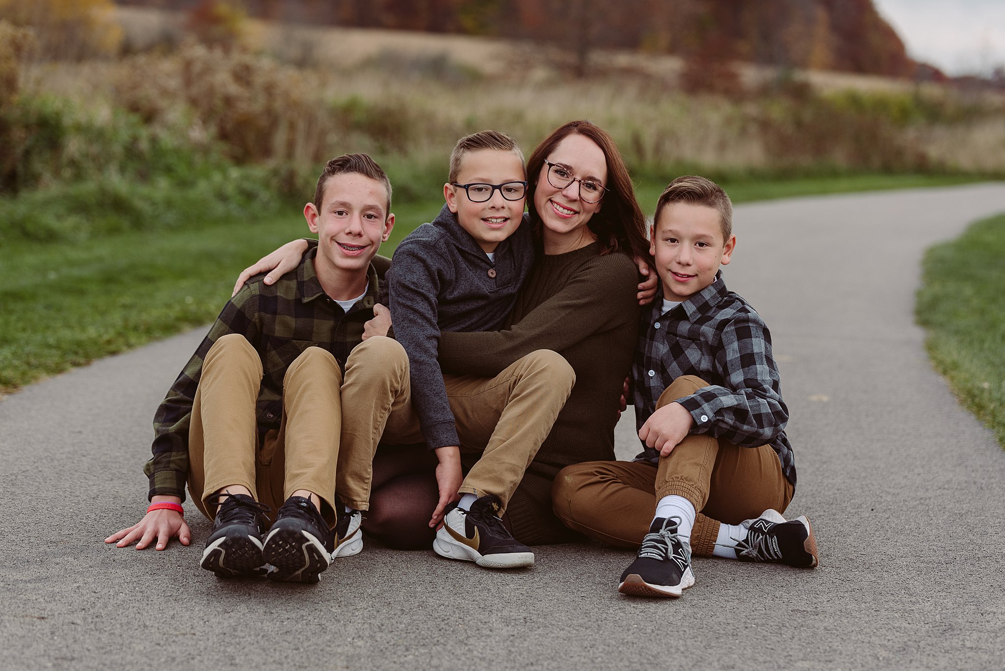 A mother sits on a park path with her three sons all around her old navy mentor