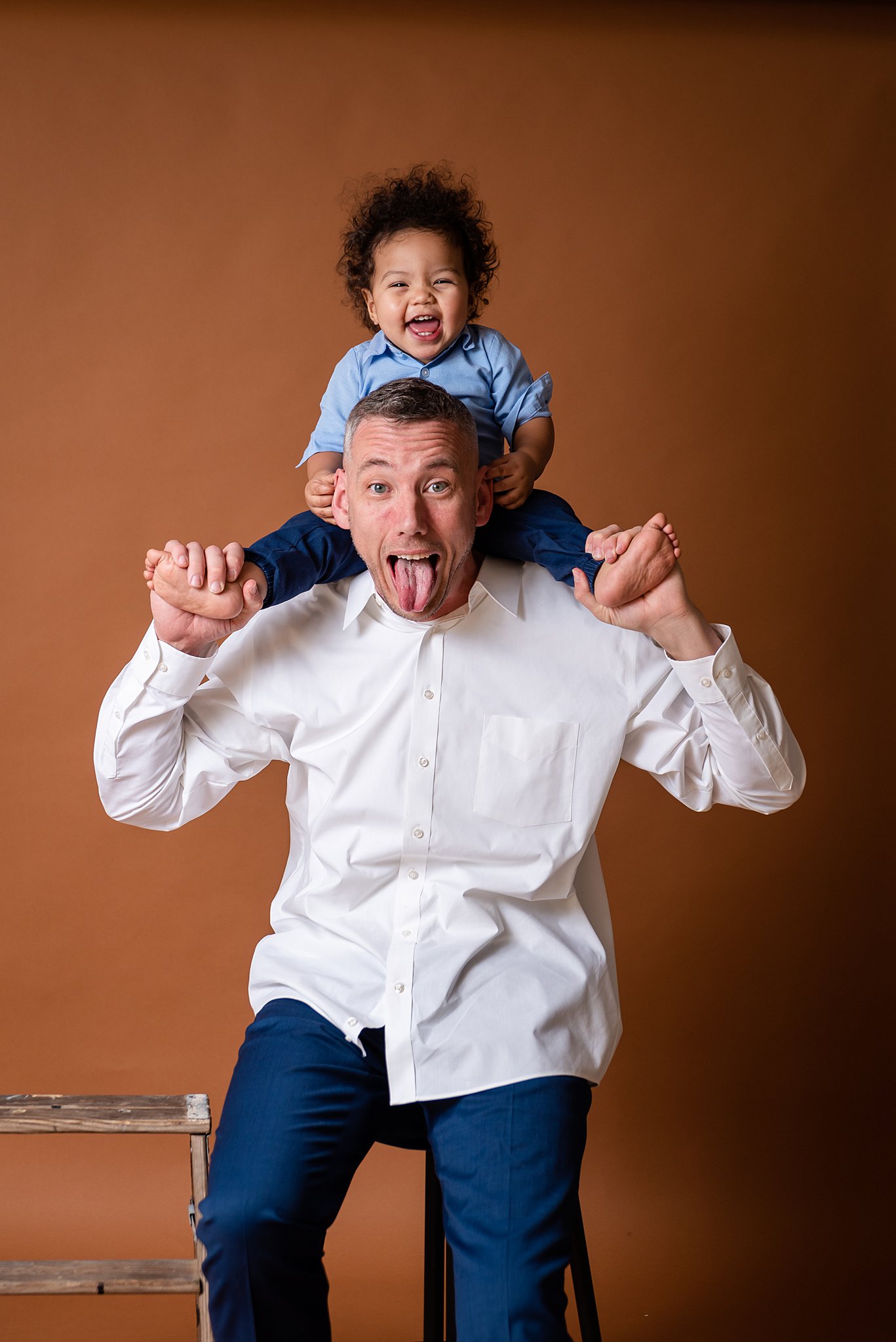 A fun dad plays with his toddler son on his shoulders in a studio