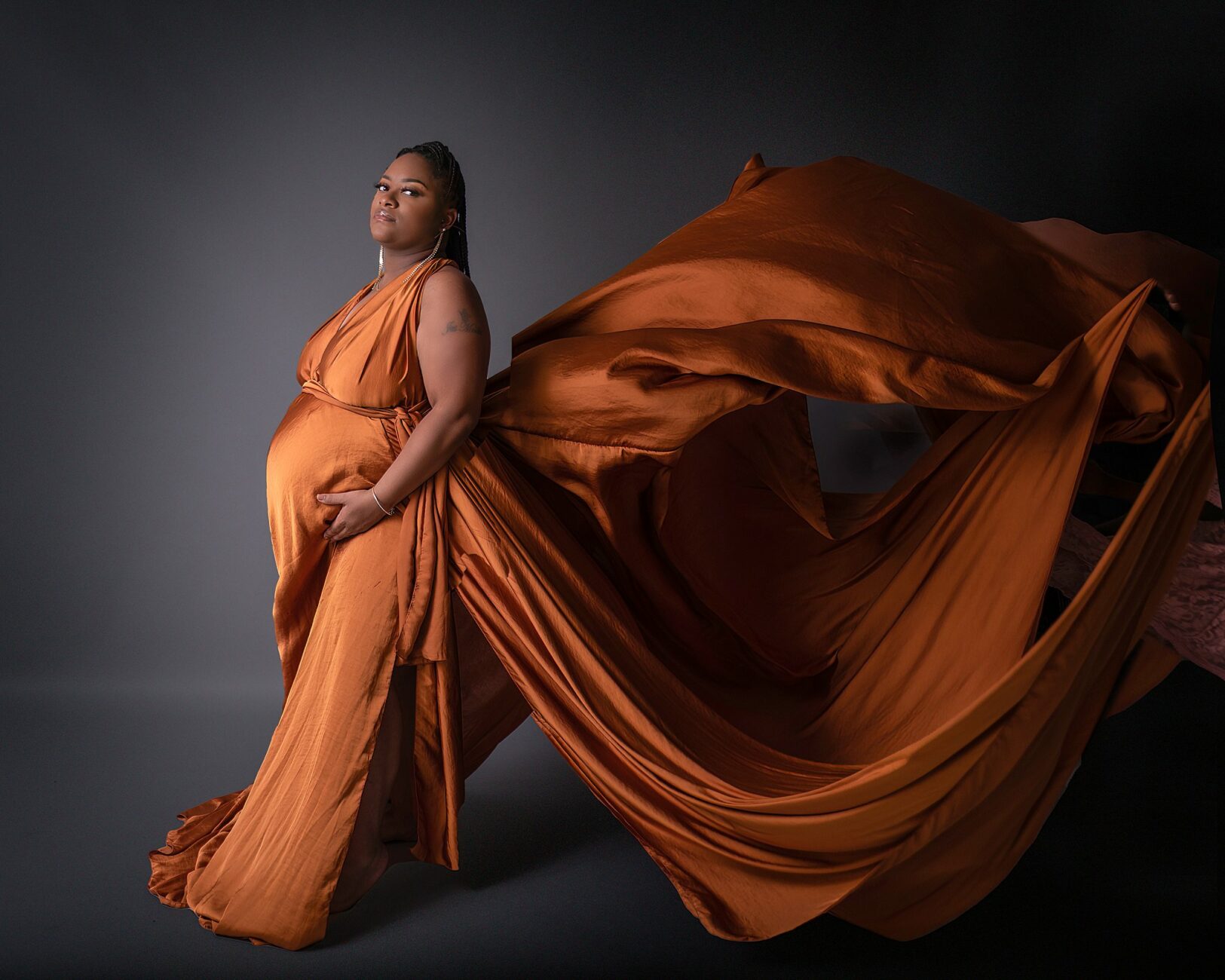 A mother to be stands strongly in an orange maternity dress that in flowing behind her pregnancy help center youngstown