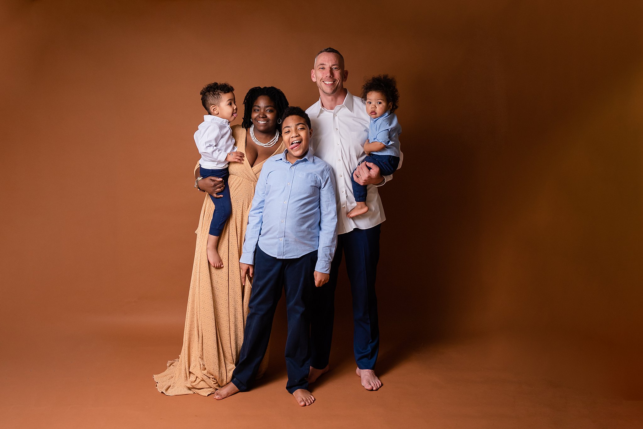 A family of five stand in a studio barefoot while the oldest son in front sticks his tongue out