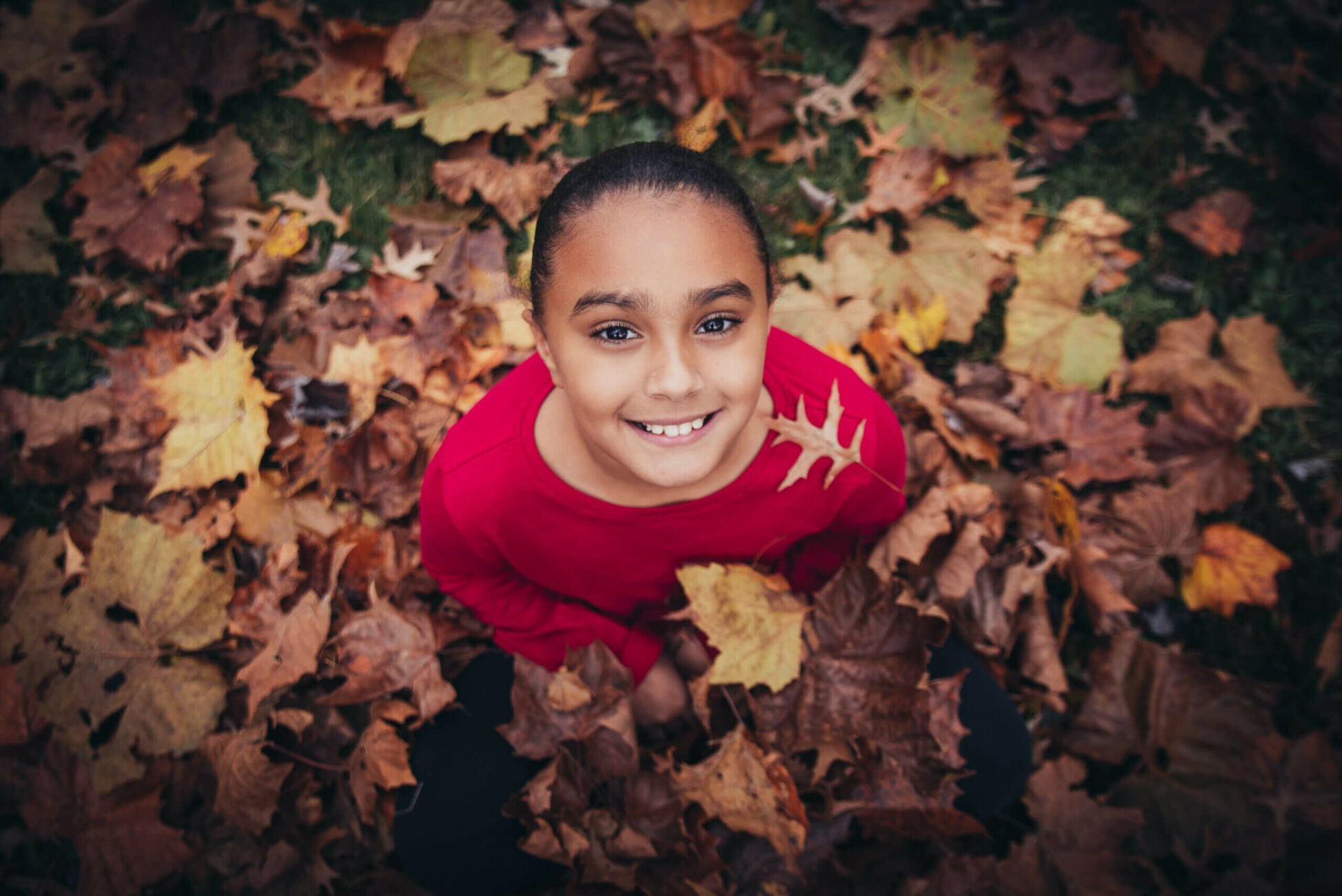 girl sitting in leaves looking up smiling at camera crocker park