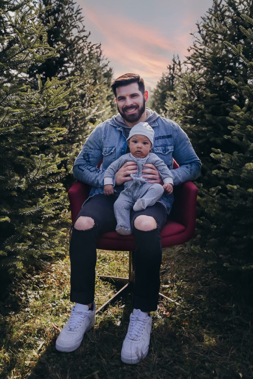 man and child sitting in a tree farm row orange village park