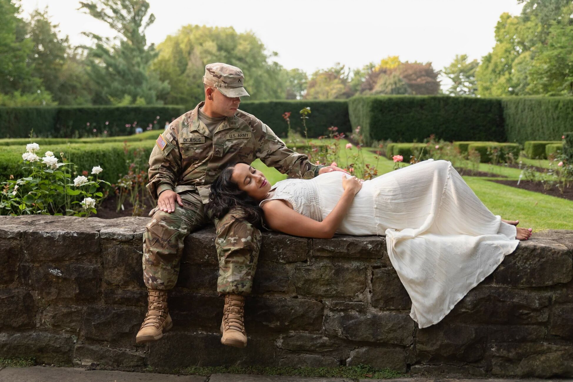 husband sitting with millitary uniform and wife lying on stone fence Maternity Clothes Cleveland Ohio