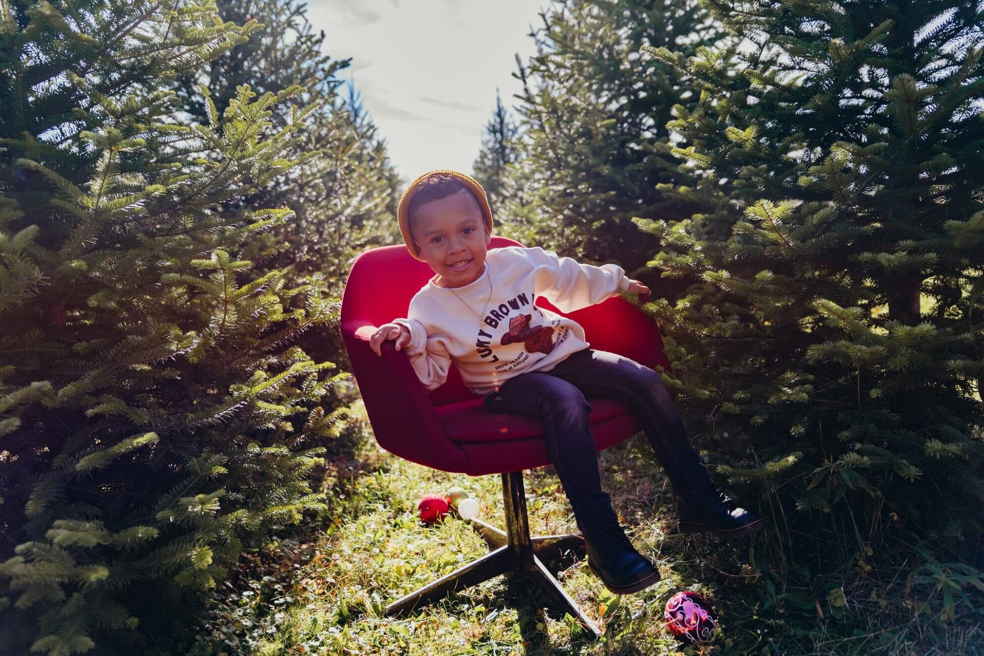 boy sitting in red chair in a tree farm for Ashton's Corner Boutique
