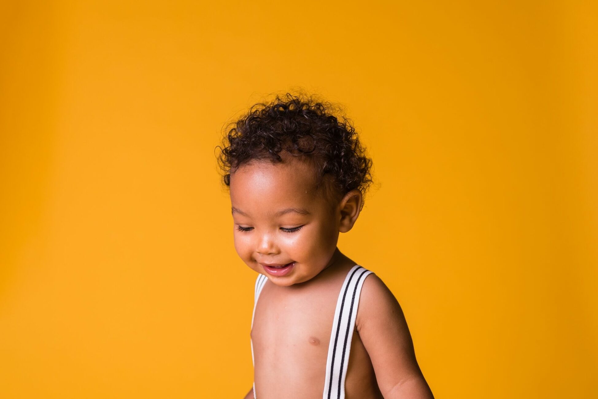 toddler smiling looking down on yellow backdrop for Baby's Away Cleveland