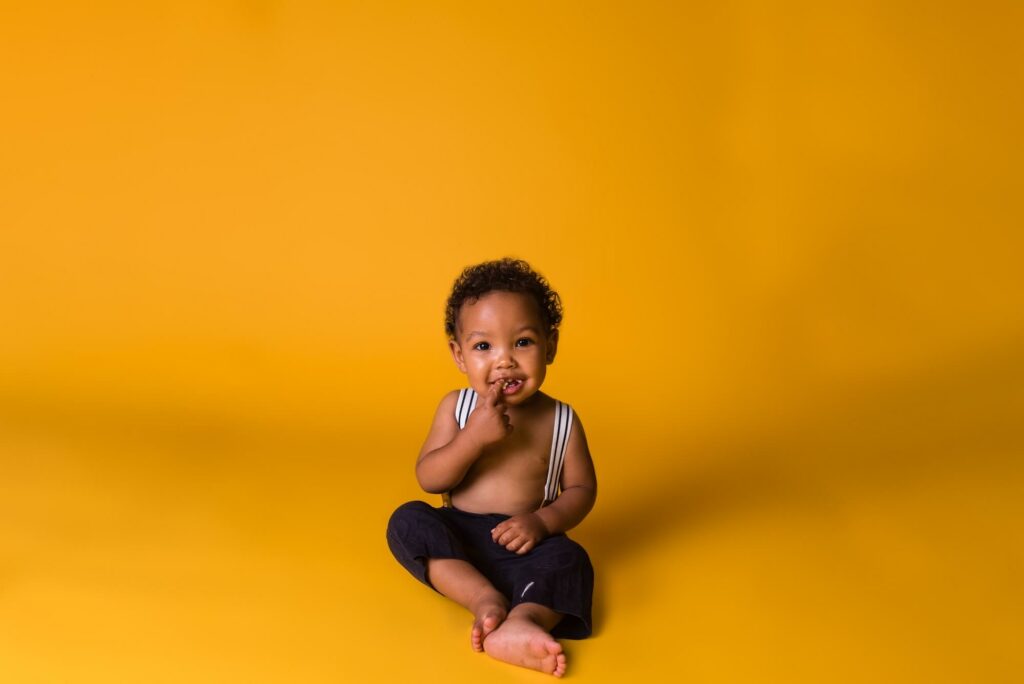 Toddler boy sitting on Yellow backdrop wearing suspenders for Baby's Away Cleveland