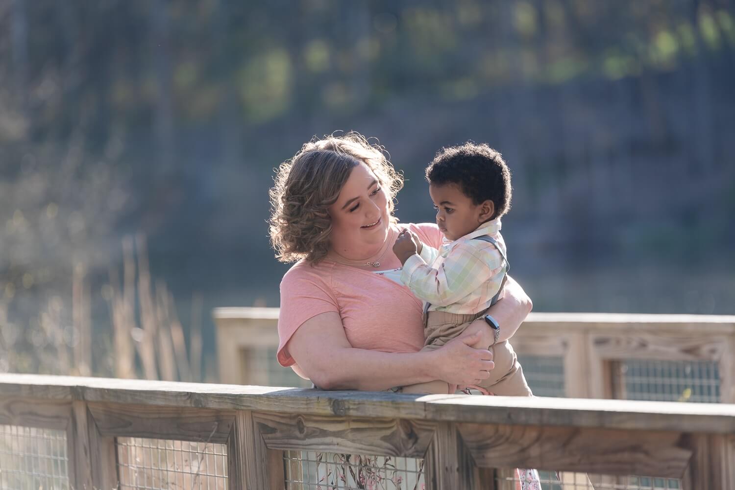 Mother holding her young child on a wooden bridge with a serene natural background Greater Cleveland Aquarium