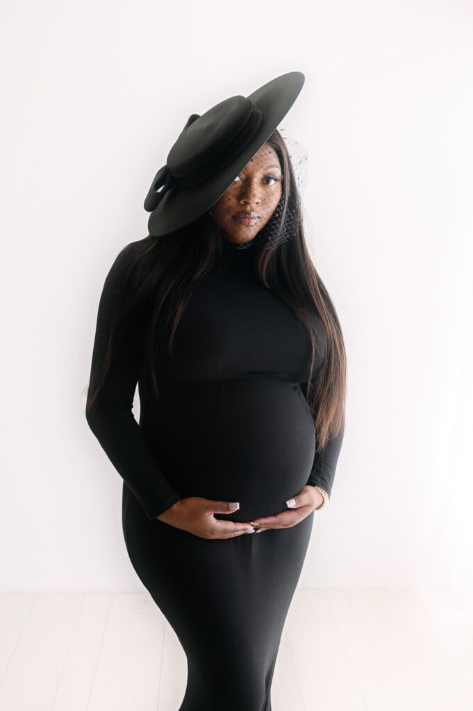 pregnant mother wearing a blavk maternity dress with a black wide fedora hat looking at camera for Pediatricians In Youngstown, Ohio