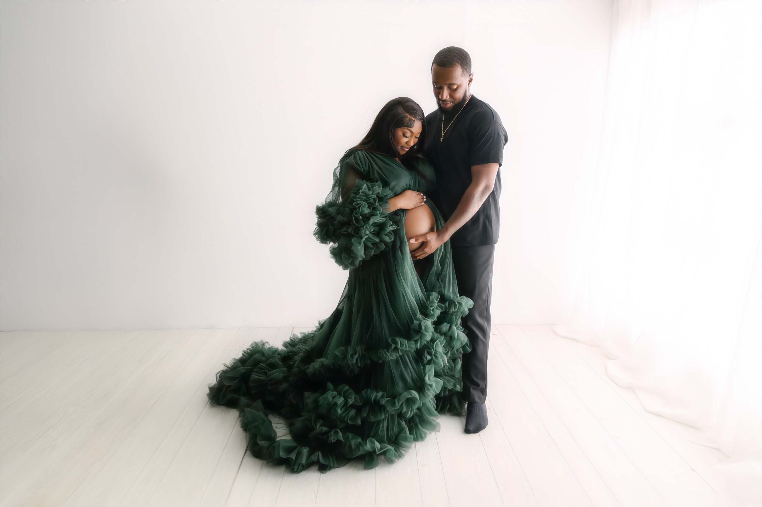 mather in a green ruffled maternity dress with father in green looking down at stomach for Pediatricians in Youngstown photography shoot