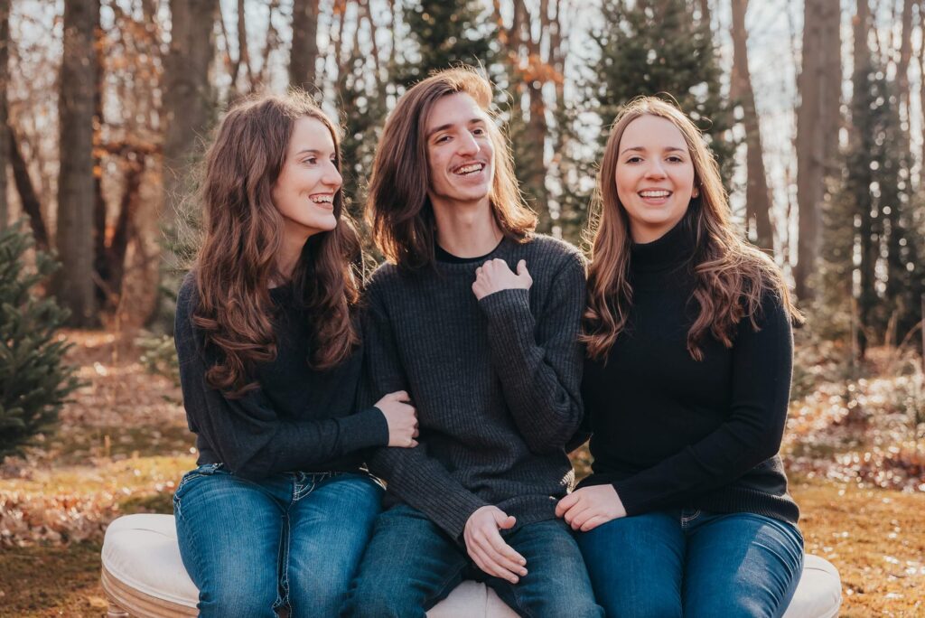 Three siblings smiling together during a family photo session at a Northeast Ohio Christmas tree farm