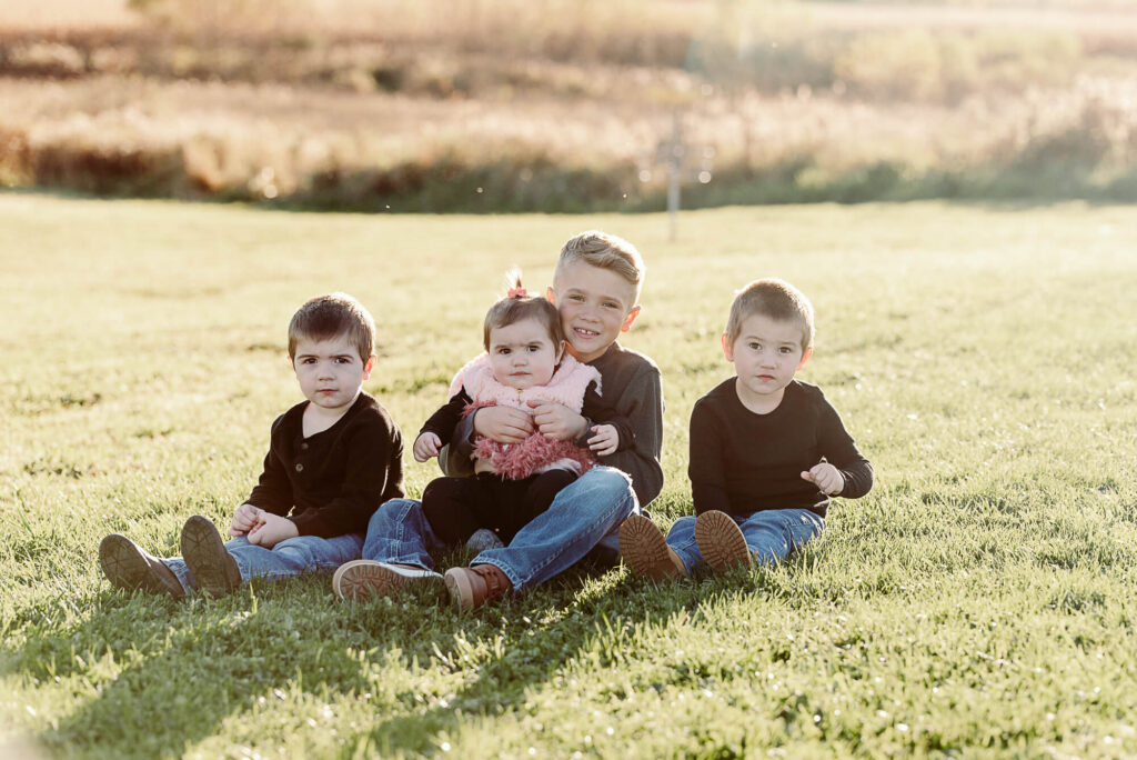 Four siblings sitting together in a field during a golden hour family photo session in Northeast Ohio