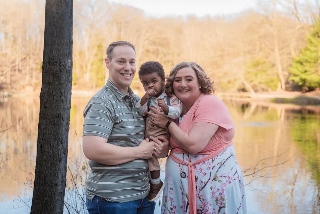 Family of three smiling together by a pond during an outdoor family photo session in Northeast Ohio