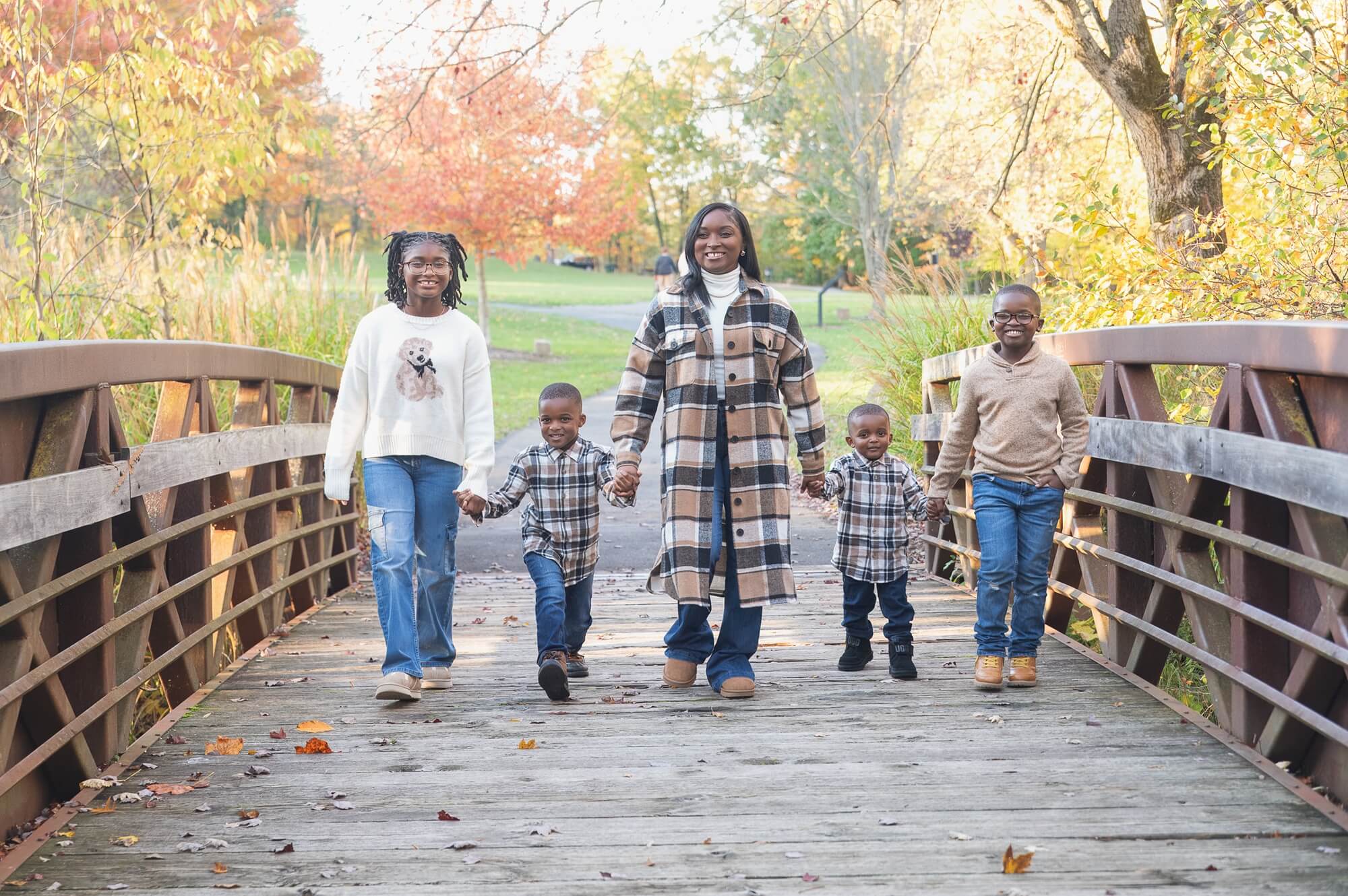 Mother and four children holding hands and walking across a wooden bridge during a fall family session in Northeast Ohio.