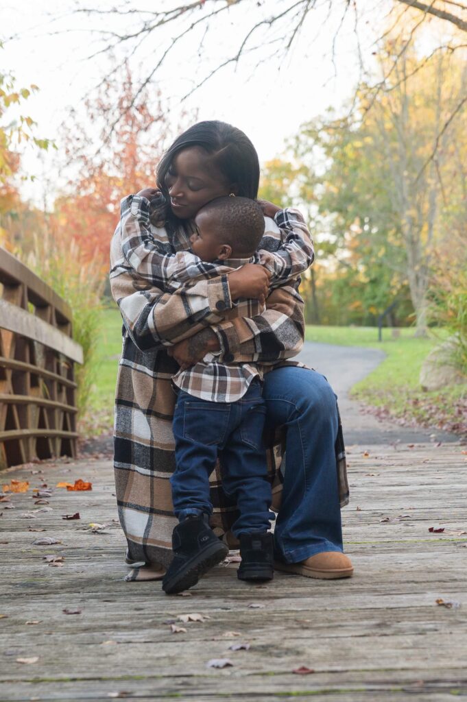 Mother sharing a warm hug with her young son during a candid fall family photography session on a wooden bridge.