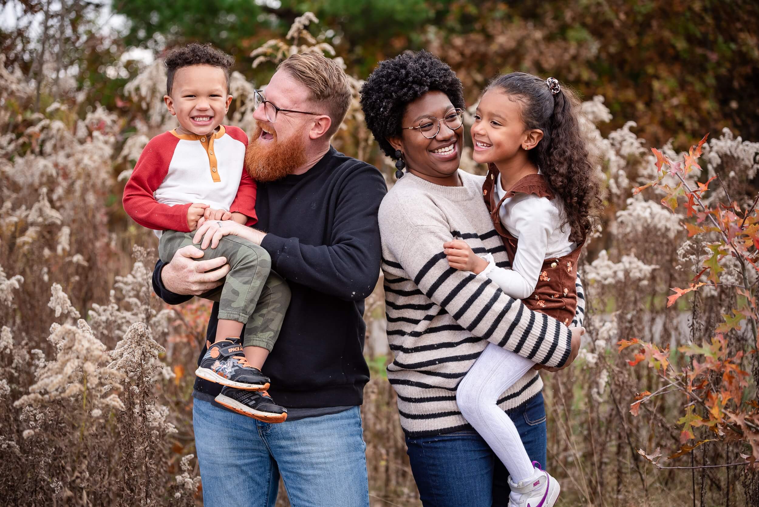 Family of four smiling and laughing together while exploring a park in Northeast Ohio during fall